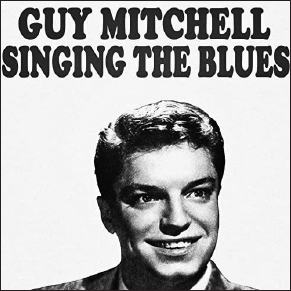 Start of image description, The record cover of the single, Singing the Blues, by Guy Mitchell. The song was released in 1956 and the cover features Mitchell glancing to his left with a fixed smile., end of image description