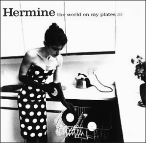 Start of image description, The record cover of Hermine’s 1982 album, The World on my Plates. Hermine Demoriane is pictured on the cover wearing a polka dot dress and elbow-length evening gloves, leaning forward to load vinyl records into a dishwasher. She is standing in front of some kitchen cabinets with a kettle plugged in on the worktop behind her., end of image description