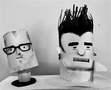 Start of image description, A pair of paper models of the heads of Adrian and his friend and fellow comedian, Phill Jupitus. The models are designed by Sam Spoons, the artist and percussionist for The Bonzo Dog Doo Dah Band. Adrian’s paper head is wearing glasses, while Phill’s has heavy eyebrows and a shock of dark hair., end of image description