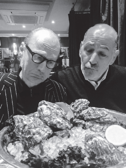 Start of image description, Adrian and David lean over the platter of empty oysters, their faces drawn in mock sadness., end of image description